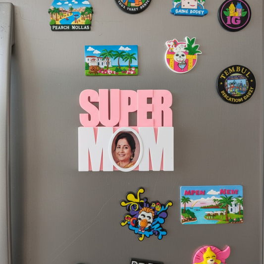 Two personalized "Super Mom" 3D photo display pieces on a white surface — one in pink and white, one in green and yellow — each featuring a woman's photo in the letter O, held by a smiling woman in a beige sweater.